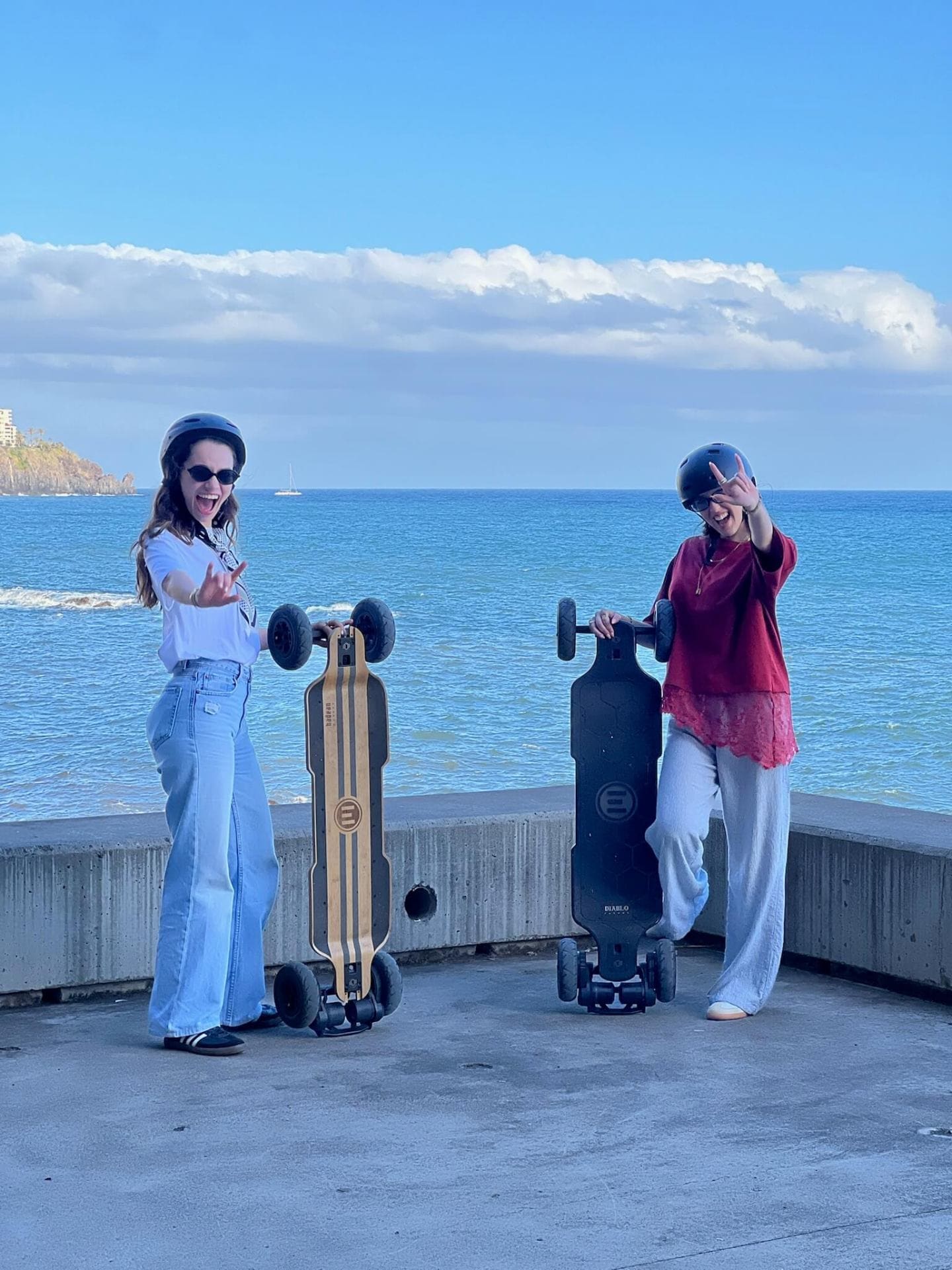 Two riders posing with electric longboards in front of the Atlantic Ocean in Madeira