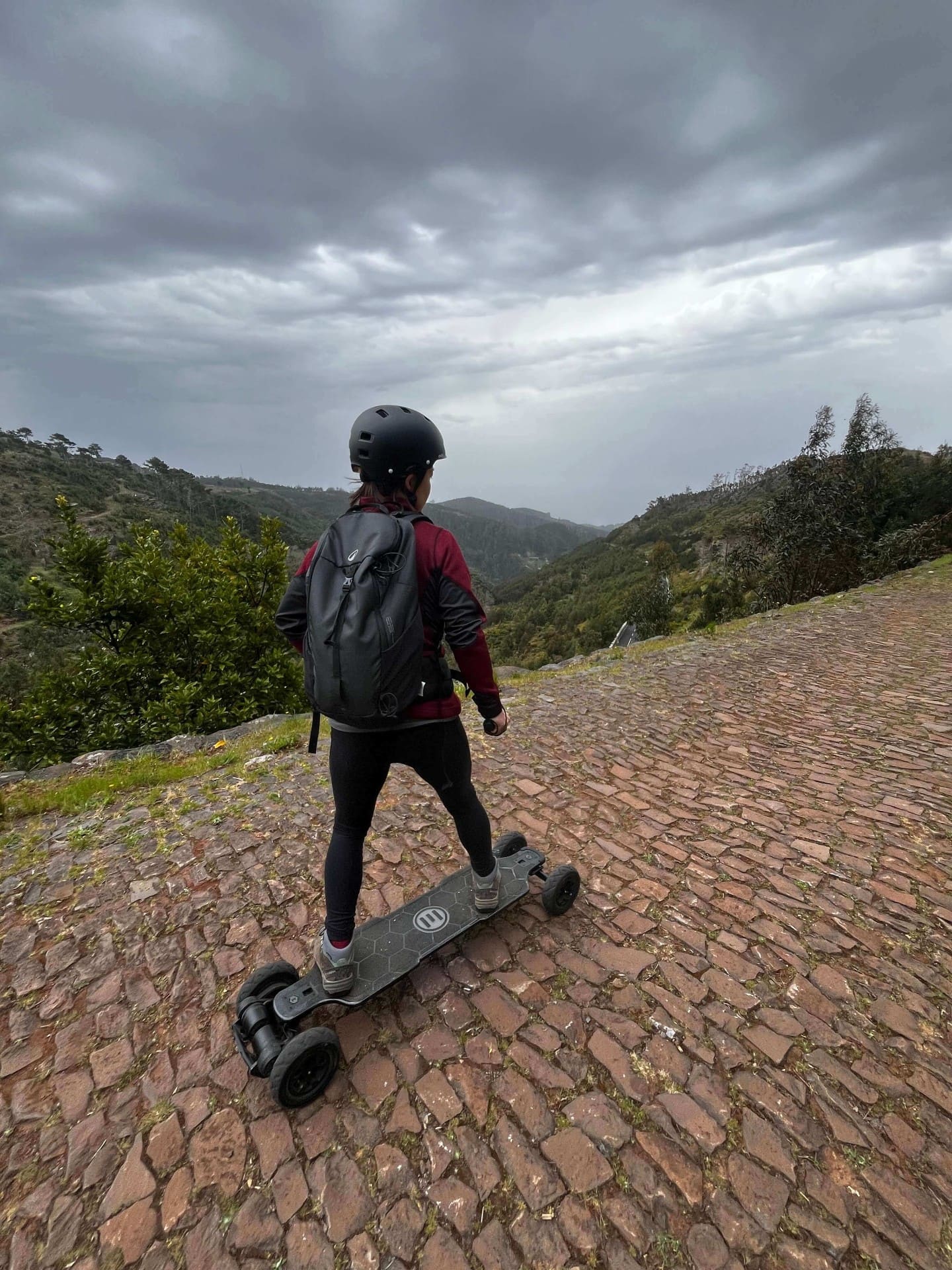 Rider on electric mountainboard descending cobblestone road overlooking Madeira valley