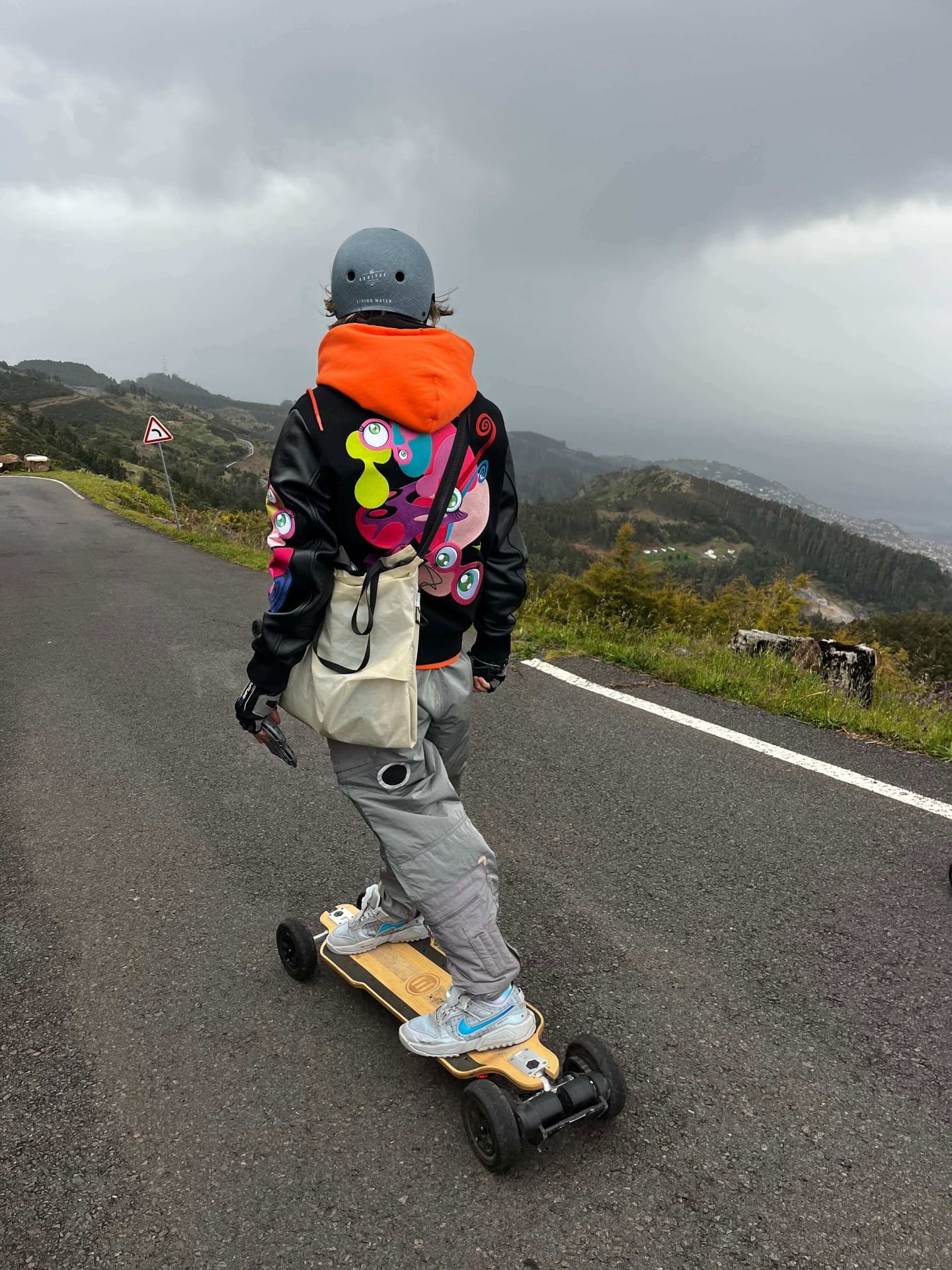 Rider in orange hoodie carving down Madeira mountain road on e-board
