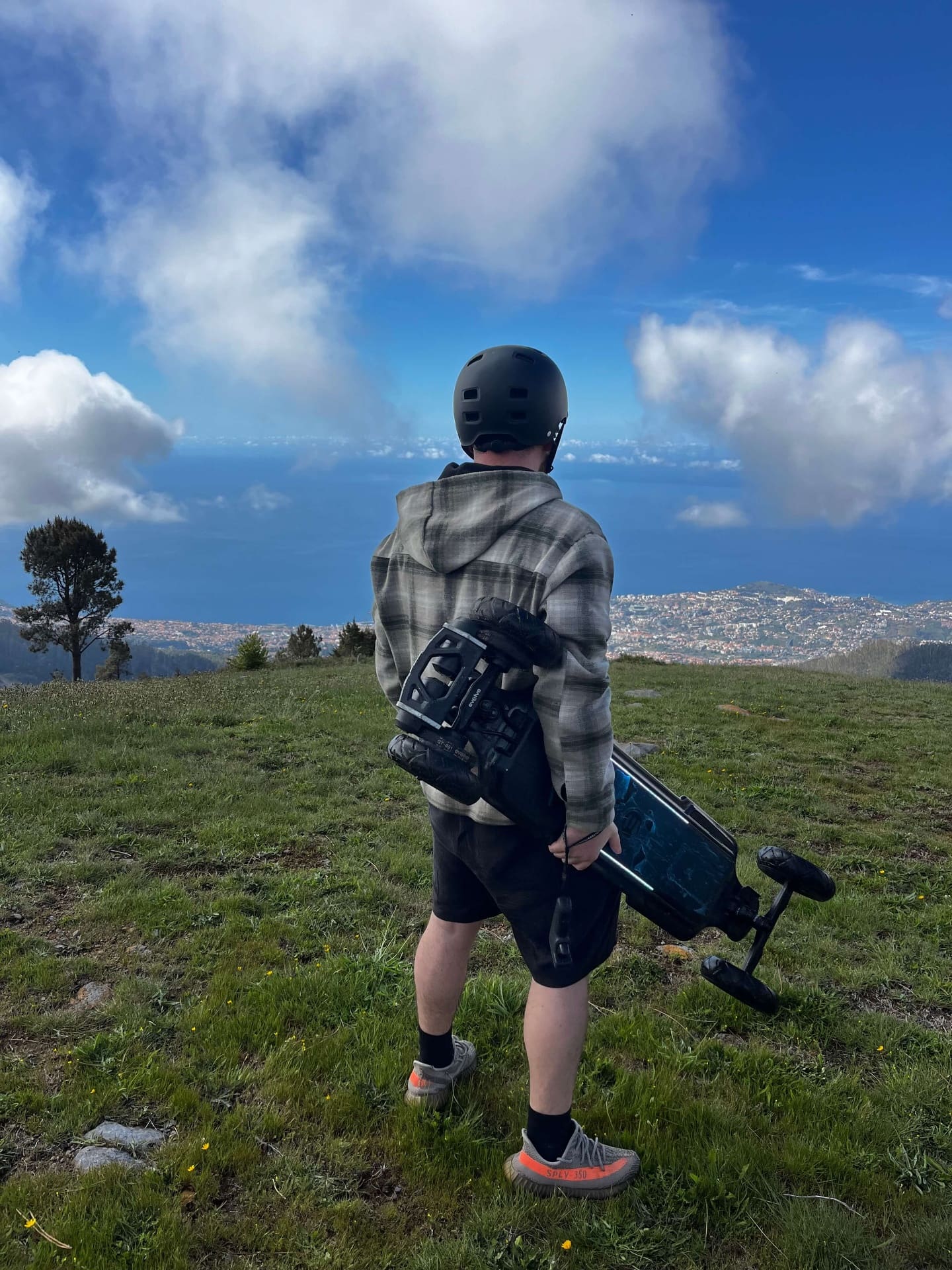 Rider carrying e-board at Madeira mountain summit overlooking Funchal and the Atlantic
